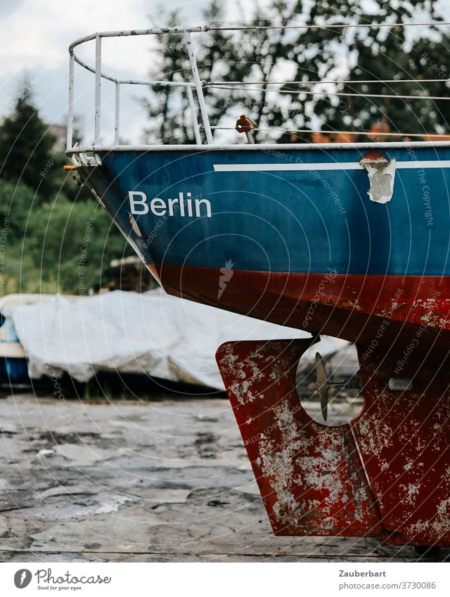 Stern with rudder of an old motorboat in red and blue on land from Berlin Old Rust Red Oar Blue corroded warehouse Boat storage Buck jacked up ship