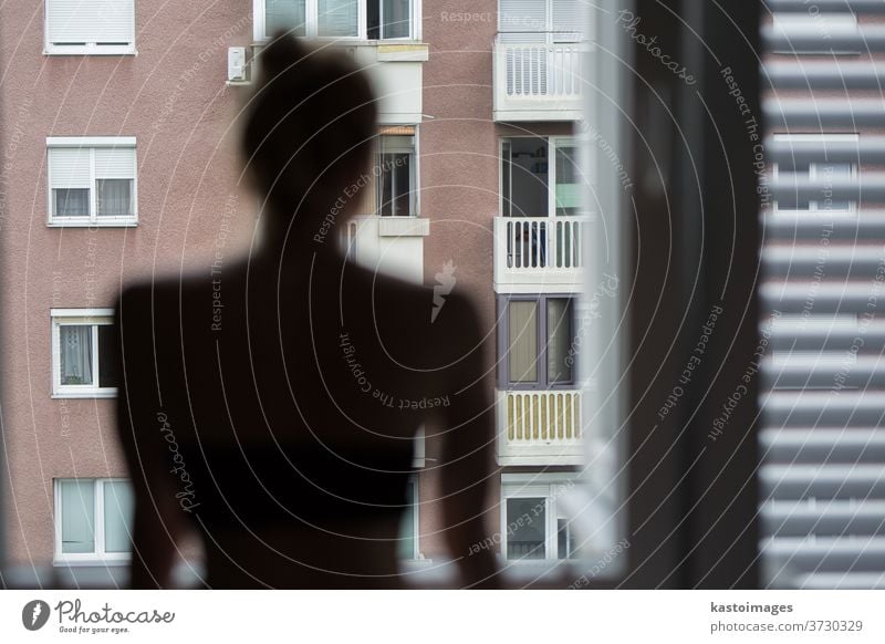 Home quarantine and social distancing during covid pandemic. Silhouette of lonley caucasian woman standing by window, anxiously looking out. Coronavirus infection, pandemics, disease outbreaks