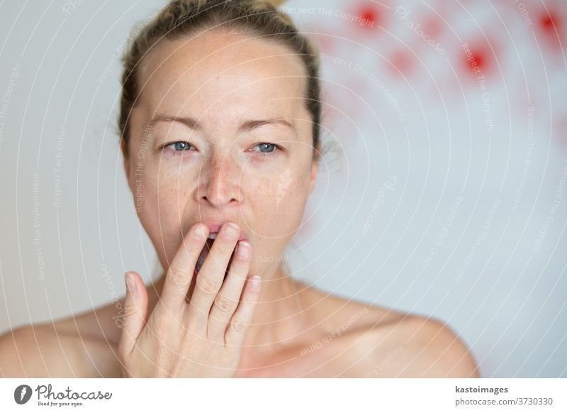 Closeup portrait headshot of sleepy young woman covering her wide open mouth while yawning by her palm. Face expression,emotion, body language concept. female