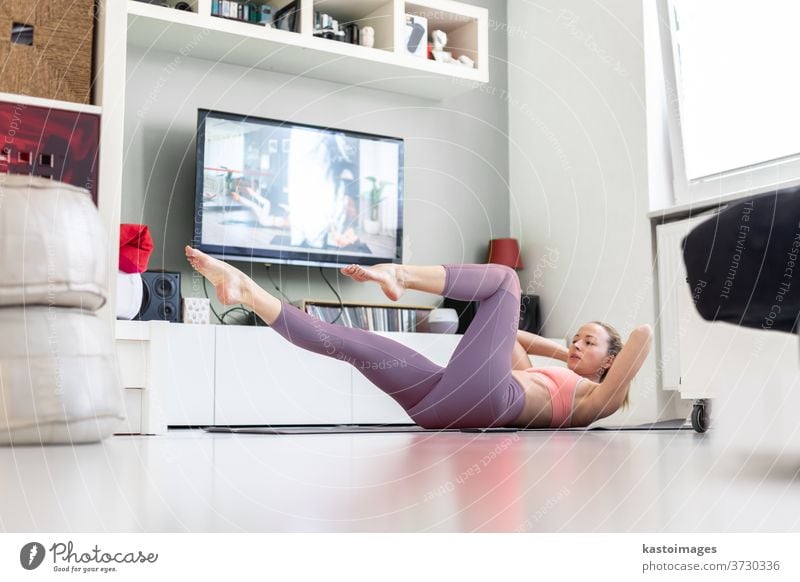 Attractive sporty woman working out at home, doing pilates exercise in front of television in her small studio appartment. Social distancing. Stay healthy and stay at home during corona virus pandemic