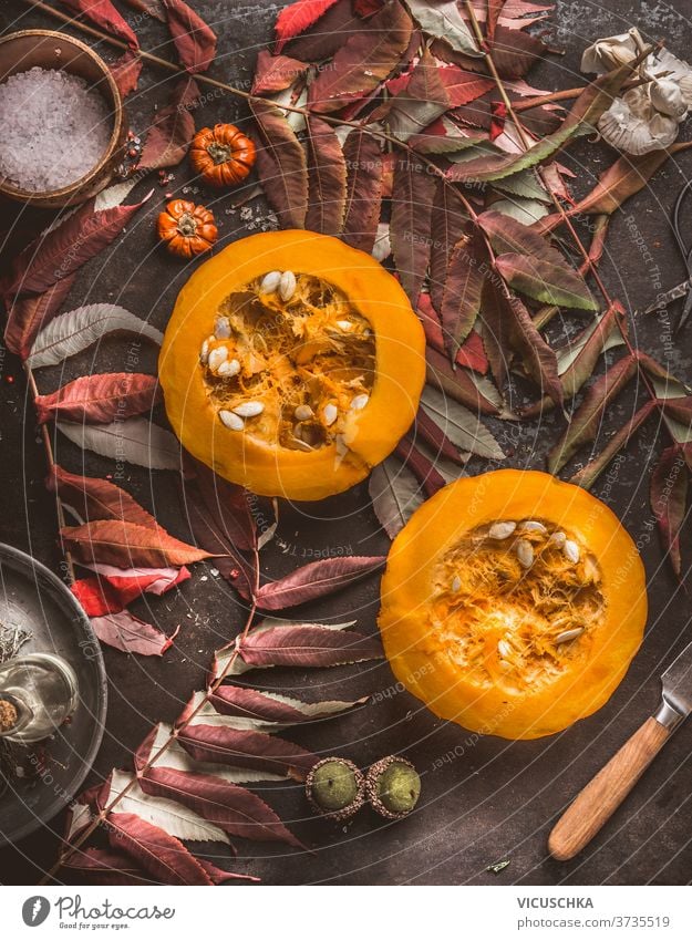 Seasonal food. Half Hokkaido pumpkin with seeds, knife and fall leaves on dark kitchen table. Autumn mood. Top view seasonal food sliced hokkaido autumn mood