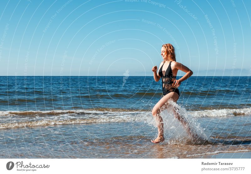 young blonde girl in a black swimsuit runs along the sand of the sea shore beauty caucasian body beautiful model female water ocean person woman summer bikini