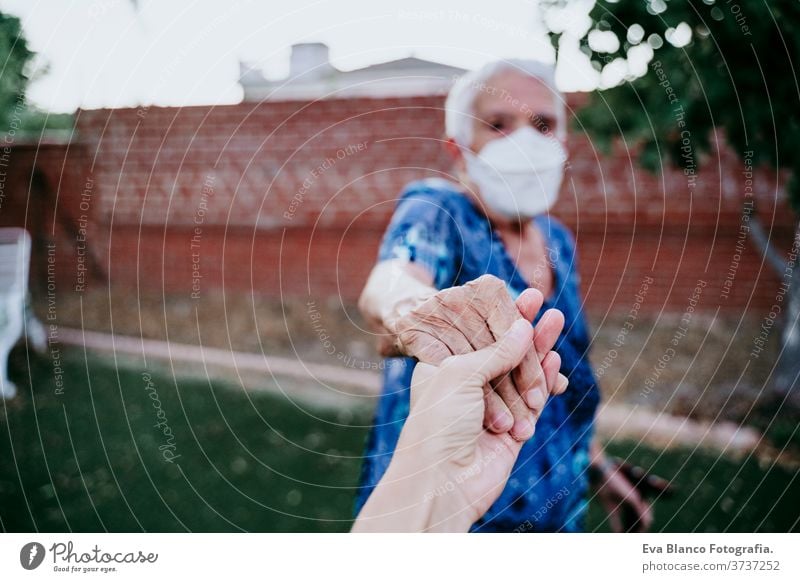 old woman wearing protective mask holding hands with unrecognizable woman. New normal concept lady young two generations follow me old lady corona virus elder