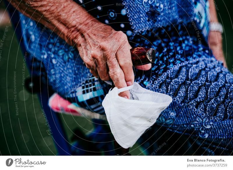 close up of old lady hands holding a stick and protective mask outdoors. new normal old woman portrait elderly home white hair grey hair mental solitude