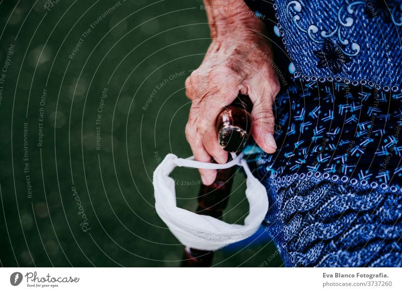 close up of old lady hands holding a stick and protective mask outdoors. new normal old woman portrait elderly home white hair grey hair mental solitude