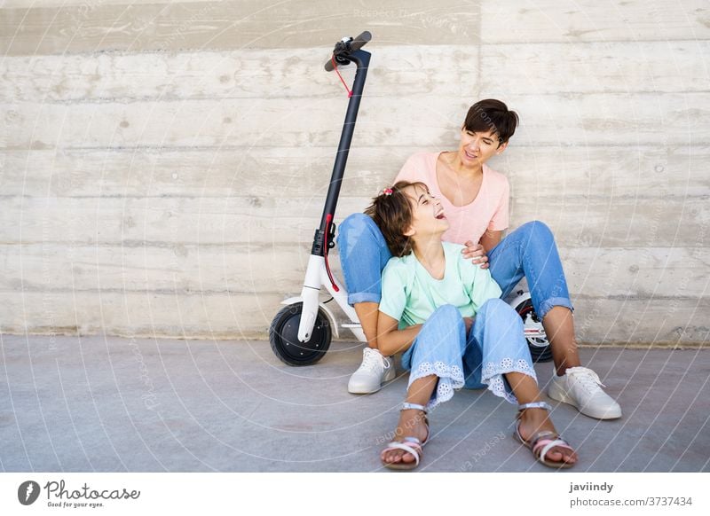 Mother and daughter sitting on an electric scooter mother girl woman eco transportation urban lifestyle modern leisure city ride female young active smile bike