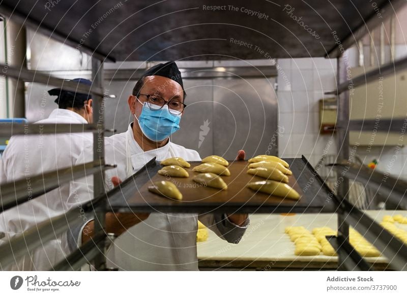 Ethnic man cooking buns in bakery pastry prepare medical mask coronavirus dough raw male ethnic tasty uniform chef professional job work food kitchen epidemic