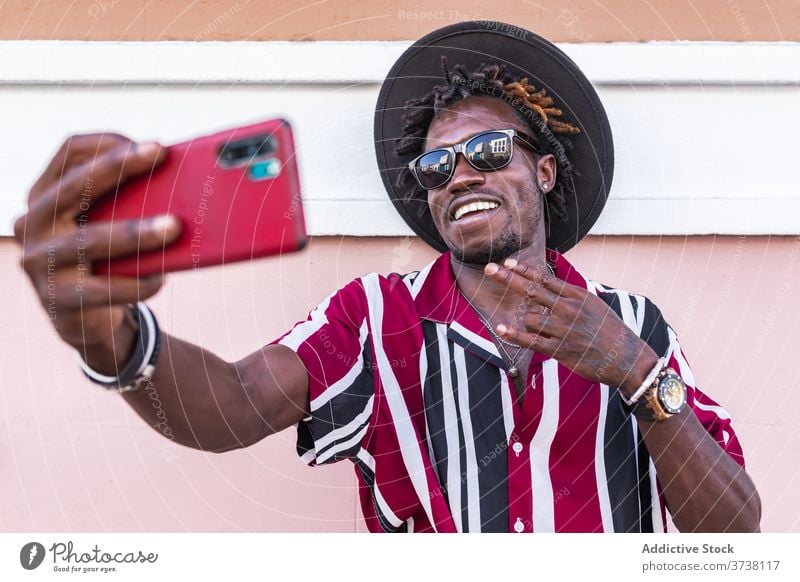 Cheerful ethnic man in stylish outfit taking selfie on street style fashion smartphone cheerful trendy funky hipster young sunglasses stripe modern male