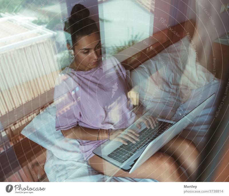 Young woman teleworking while making videocall on laptop and sitting on bed. Young student in online class. indoors computer people at home technology internet