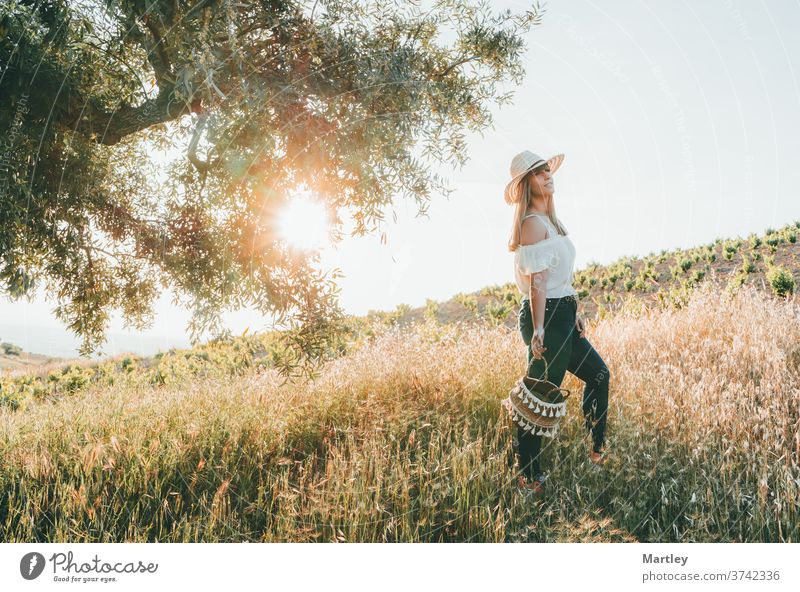 Young woman with a straw hat and a basket walking through the field at sunset in summer. Concept of freedom, tranquility, nature, ecology, green world and happiness.