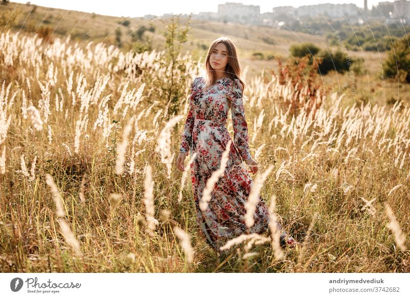 beautiful young woman in dress in field at sunset. stylish romantic girl with long hair having fun outdoors. summer beauty nature free meadow model fashion