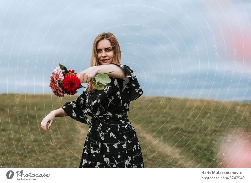 Woman holding flowers in hand outdoors in nature adult attractive beautiful beauty cute dress face fashion female field flower wreath freedom girl grass green