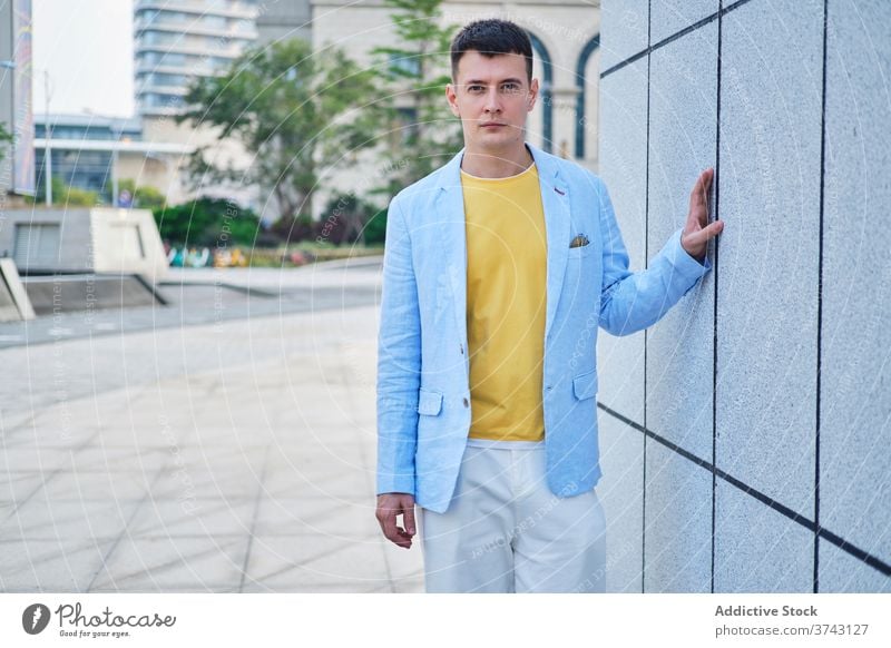 Young man on the street leaning on wall and looking at camera adult portrait background blue yellow male lonely minimal mood sense style think vintage depth