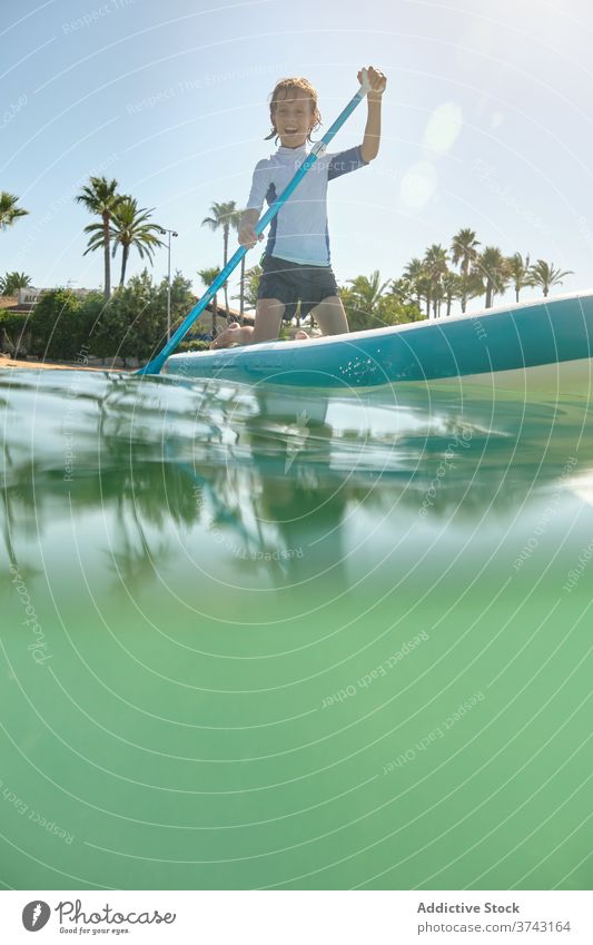 Boy on his knees on a paddle surfboard rowing in the middle of the sea lifestyles race teenage laughing ride position carefree balance enjoyment holidays up