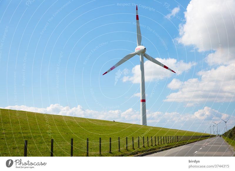 Wind turbine for renewable power generation in front of a dike on the North Sea coast, long straight road. Wind turbine wind power Wind energy plant