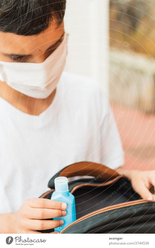 Schoolboy puts sanitizer and mask into her backpack. Student safety after covid-19 pandemic. Back to school after coronavirus outbreak. Child alcohol