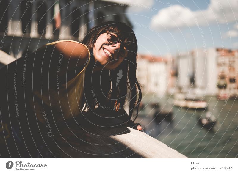 Woman leans over the railing of the Rialto Bridge to hold her face in the sun tourist Sun Venice Laughter Italy Channel Port City Joy Eyeglasses brown-haired