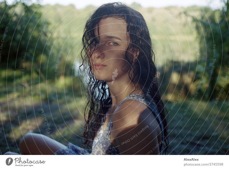 Analogue portrait of a young woman at a lakeside in nature with light and shadow through trees Beautiful weather Moody Self-confident Dress wet hair Lake Woman