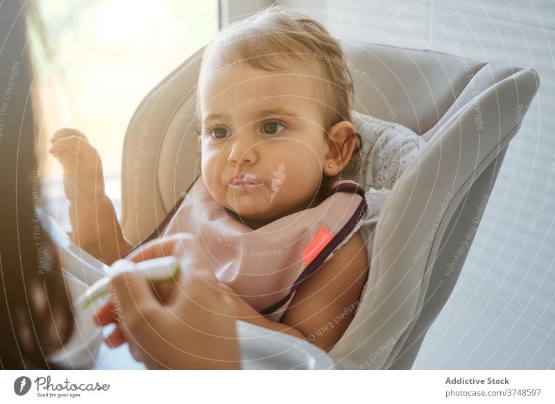 Anonymous mother feeding a baby with a bib innocence sharing infant motherhood togetherness wellbeing bonding mouth toddler concentration dining daughter indoor