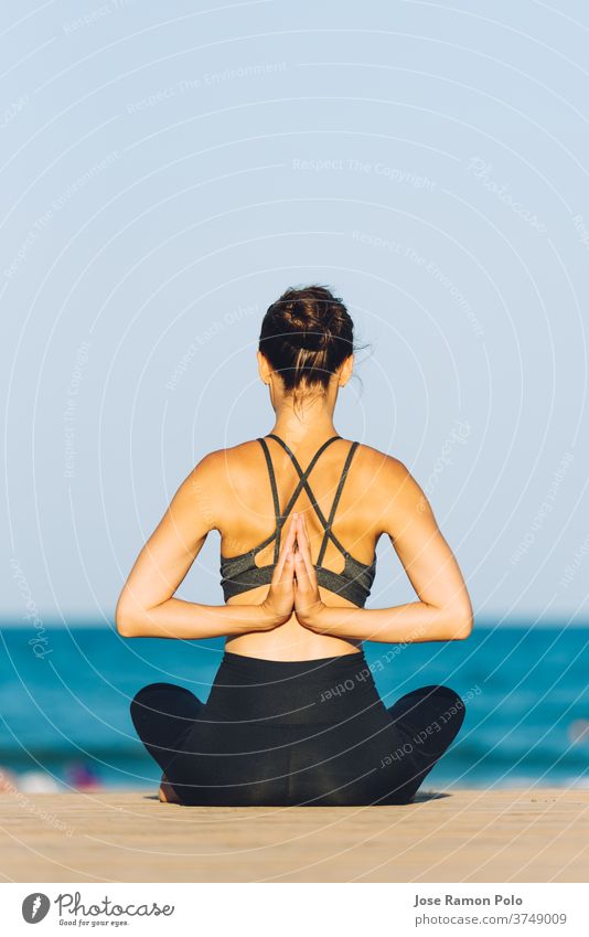 young woman from the back doing yoga in front of the sea on a sunny day meditation health sand sitting people fit relaxation sunshine tranquil deserted person