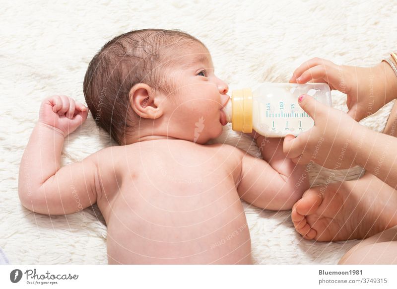 Young sister feeding little newborn brother by milk bottle on bed Caucasian face nutrition eating holding girl happy adorable help baby backdrop beautiful care