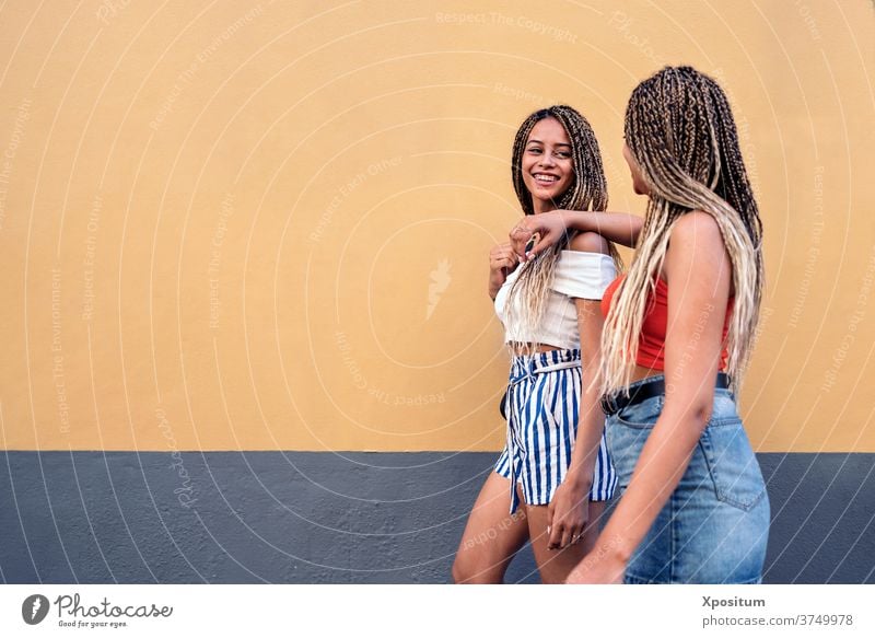 Cool Sisters Having Fun side view sisters walking street braids ethnic racial looking at each other smiling urban women portrait two women background city