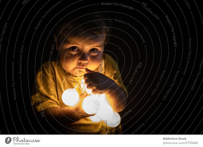 Cute boy playing with garland at home child illuminate glow festive little curious dark apartment room kid joy childhood innocent cute adorable light holiday