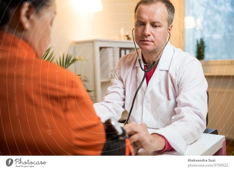 Doctor measuring blood pressure of female patient in hospital office. Sick senior woman having a doctor appointment. Close up care support old people hand