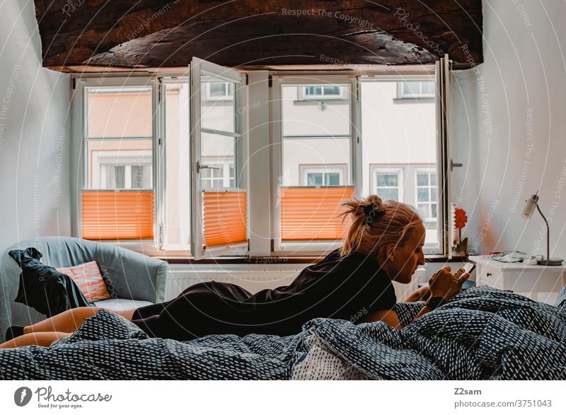 Young woman in bed with the Smarphone Bed at home Relaxation relaxation dwell Cozy Window Light Old building Blonde long hairs pretty Lie Cellphone smarphone