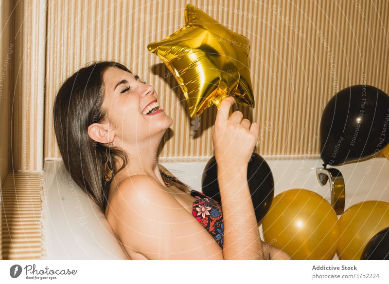 Young woman in bathtub with balloons after party tired festive celebrate holiday event laying down young female funny rest occasion xmas color new year relax