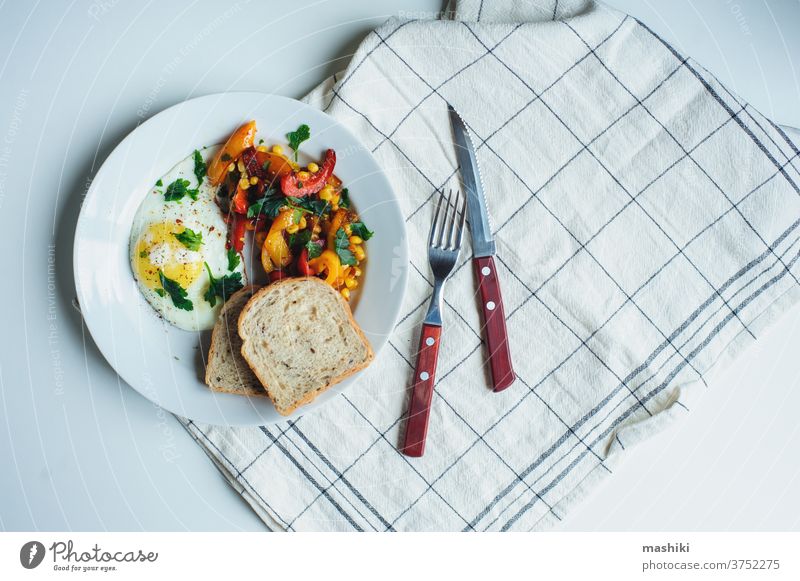 tasty vegetarian farm style breakfast - fried egg with baked sweet peppers and corn with parsley and whole grain bread served on white plate vegetable food