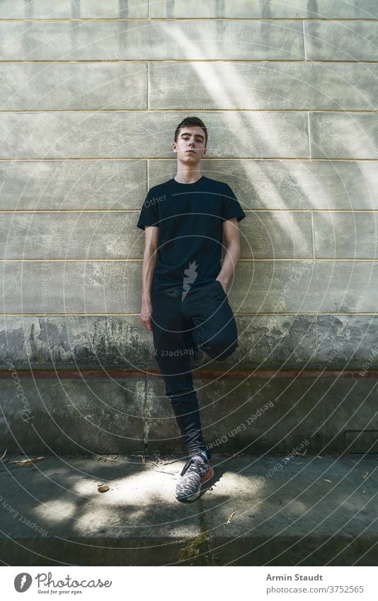 portrait of a cool, standing young man who is leaning against a wall grunge confident serious sportswear dirt outdoor teenager looking male beautiful casual