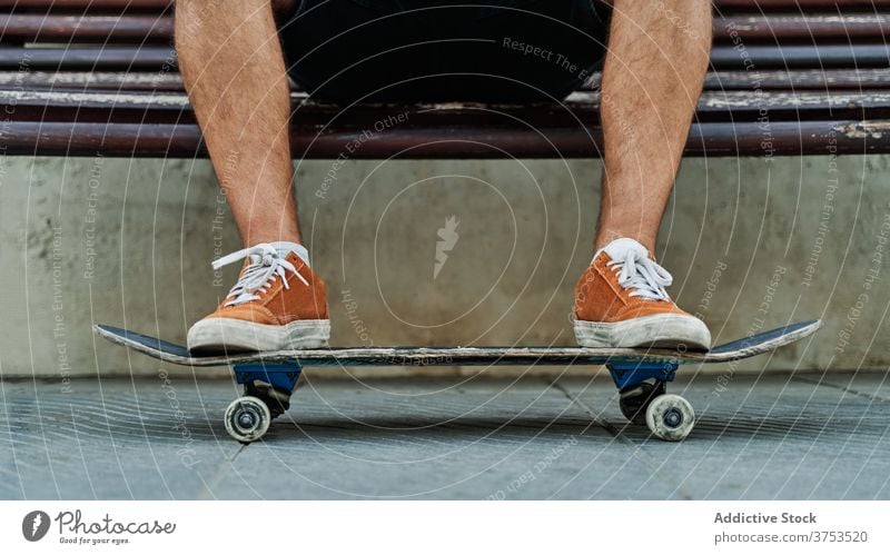 Crop skater sitting on bench in city urban skateboard man relax style street cool generation male young shabby wooden rest trendy hobby town modern hipster