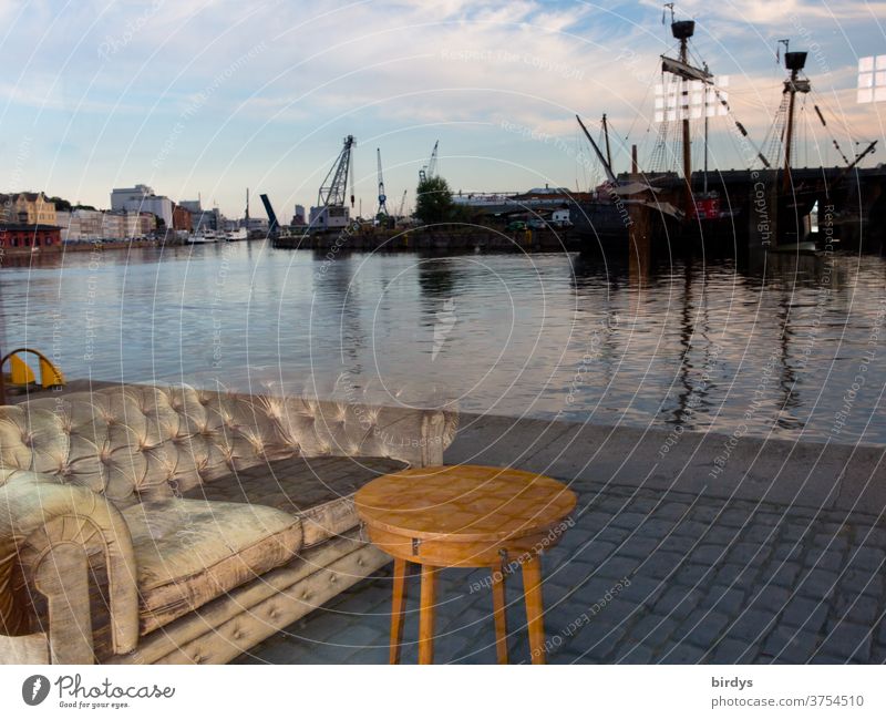 A sofa with a table stands at the quay of the port of Lübeck. Deceptive reflection in a window pane Harbour Sofa Table Reflection ships cranes port facility