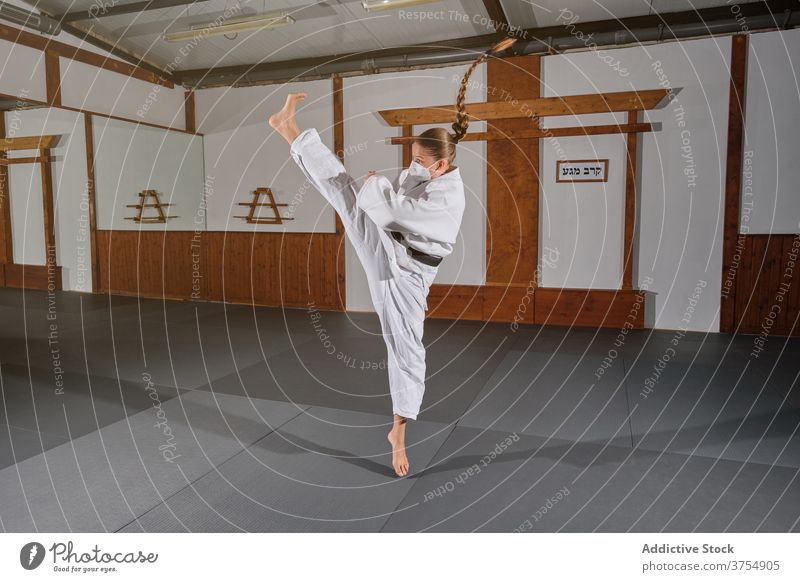 Woman with a white kimono kicking in the air posture balance powerful trainer wellbeing practice skill strength sports uniform wellness position confident