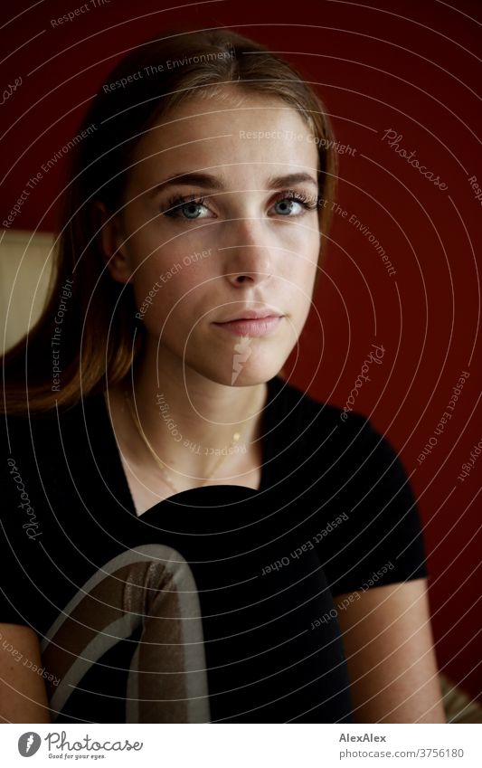 Young woman in a beige armchair in front of a red wall Day Aesthetics focused Force blue eyes décolleté great Definitive Calm athletic Skin Uniqueness feminine