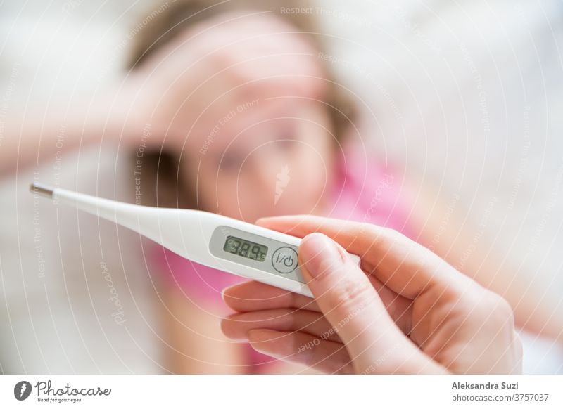 Close-up thermometer. Mother measuring temperature of her ill kid. Sick child with high fever laying in bed and mother holding thermometer. Hand on forehead.