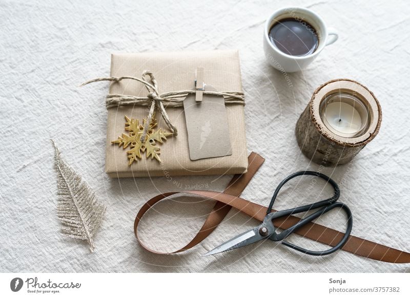 Christmas wrapped present with scissors and a cup of coffee on a beige background Gift Claw Packaged Coffee Cup Band retro style Beige Linen cloth Close-up