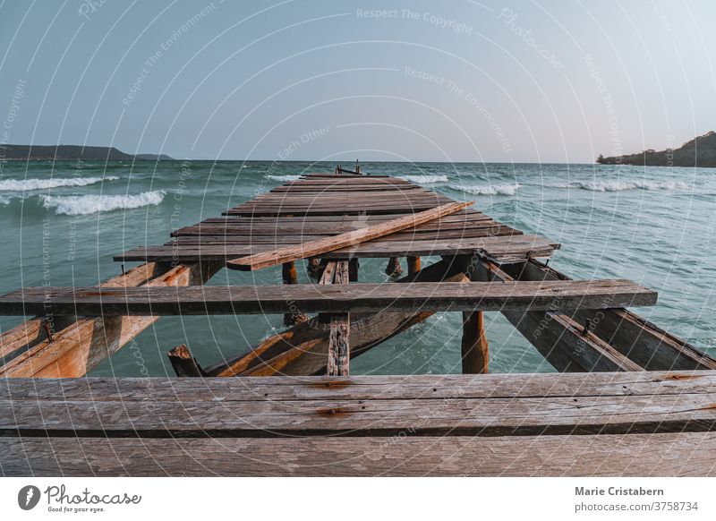 Cinematic summer scenery of a broken wooden pier in against the vast blue sea at Sok San Beach Koh Rong Island in Cambodia showing concept of supporting mental health, social isolation and social distancing during the covid-19 pandemic