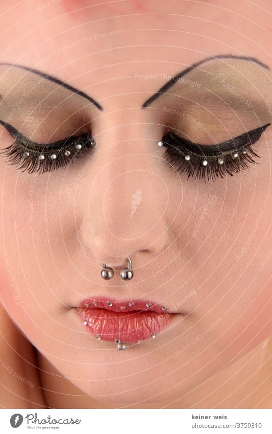 A made-up woman's face in close-up with nose ring and piercing and pearl jewellery on eyes and lips Face of a woman Woman Jewellery Face Jewellery