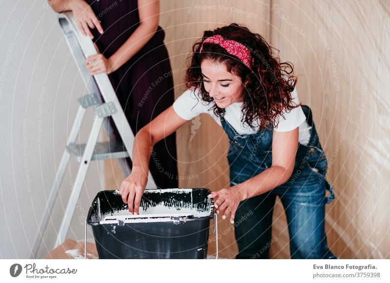 happy lesbian couple painting the room walls with white color. Do it yourself and new home concept friends two renovating house do it yourself casual women