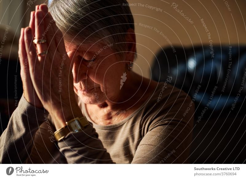 Senior woman praying at home female house sunlight aged calm indoors mature person adult care elderly senior old oap faith prayer hands pensioner morning living