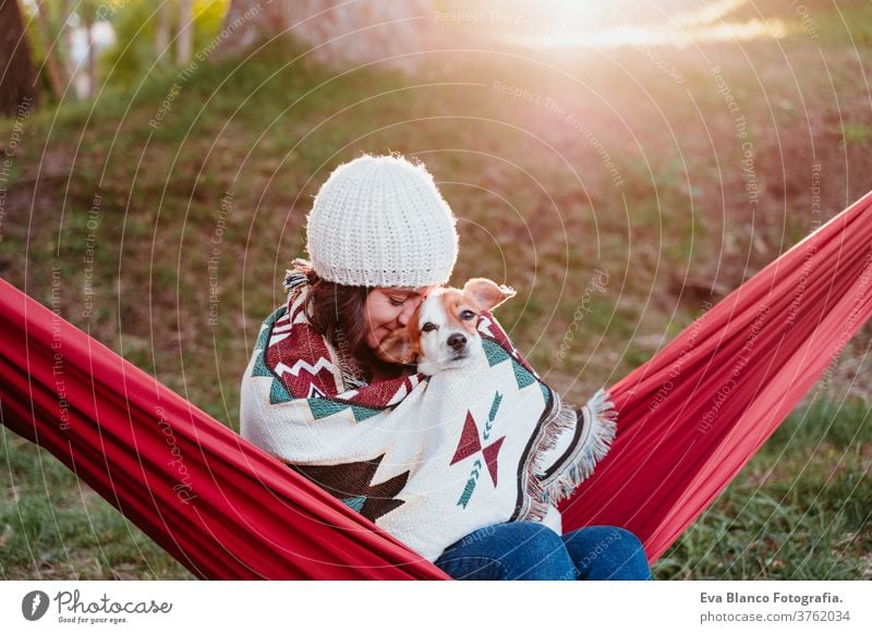 young woman relaxing with her dog in orange hammock. Covering with blanket. Camping outdoors. autumn season at sunset lying hammock jack russell pet nature park