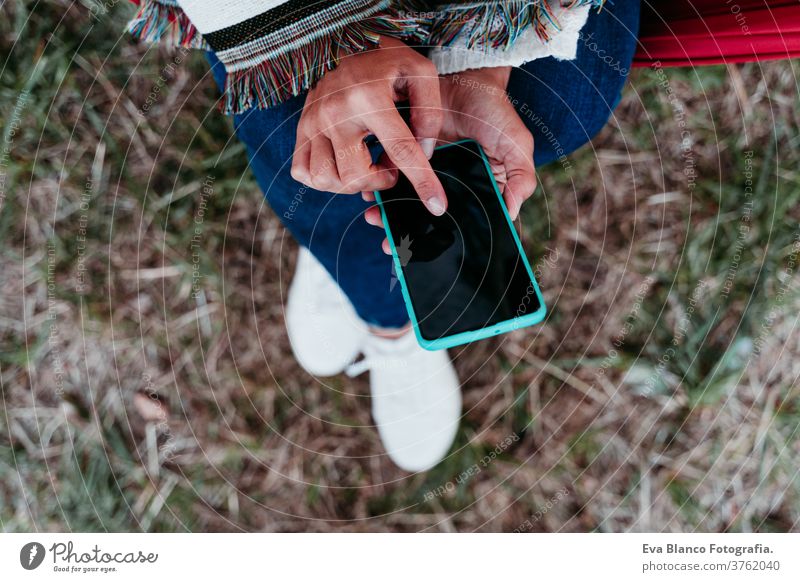 top view of woman relaxing in hammock at sunset. autumn season. camping concept mobile phone technology internet app connection using lying outdoors nature