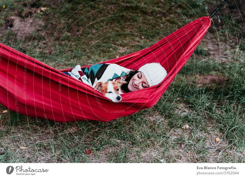 young woman relaxing with her dog in orange hammock. Covering with blanket. Camping outdoors. autumn season at sunset lying hammock jack russell pet nature park