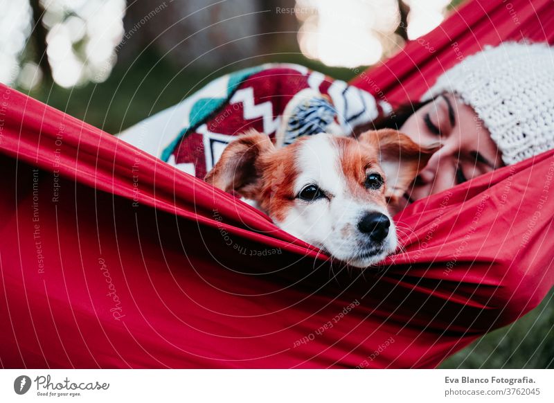 young woman relaxing with her dog in orange hammock. Covering with blanket. Camping outdoors. autumn season at sunset lying hammock jack russell pet nature park