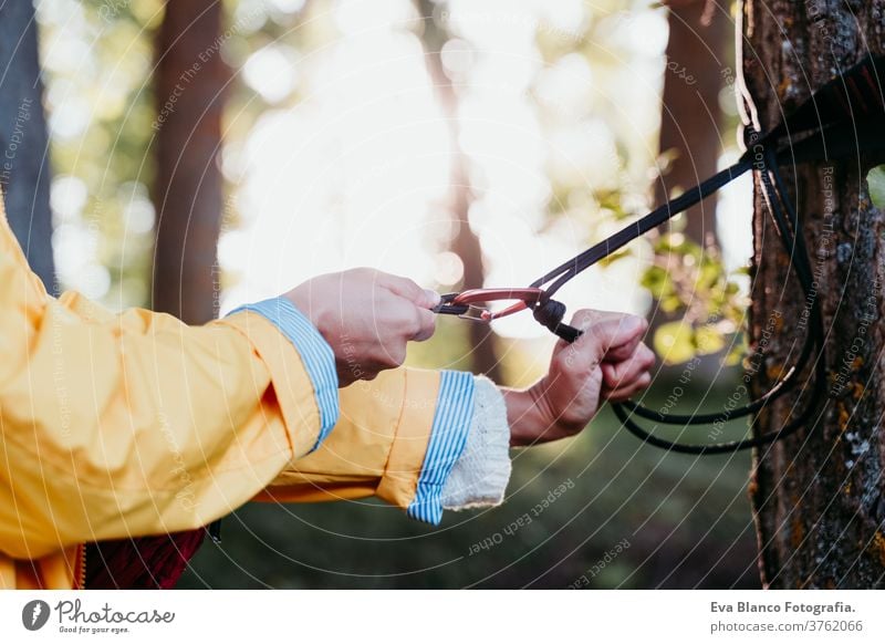 unrecognizable woman wearing yellow raincoat preparing hammock to relax. Camping outdoors. autumn season sunset orange park caucasian happy campground morning