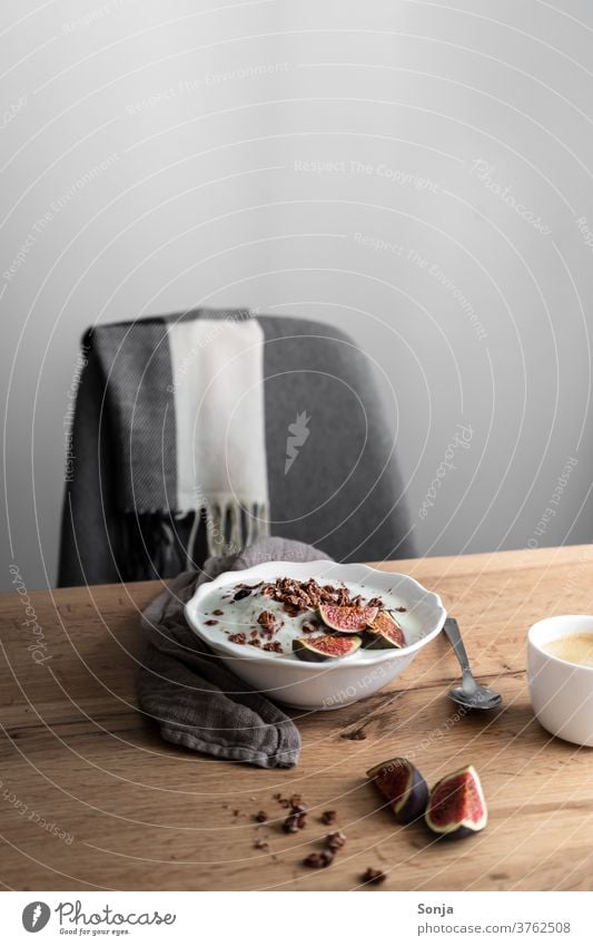 Breakfast table with granola, yoghurt and fresh figs and an armchair. White wall, healthy food. Yoghurt Fig Fresh Cereal Coffee Cup Spoon Interior shot