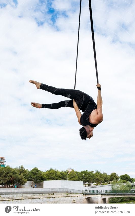 Flexible man training on aerial straps gymnast gymnastic hang perform flexible fit park male workout exercise energy athlete sport healthy sportswear effort