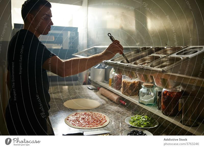 Chef smearing tomato sauce on pizza chef dough pour cook table ladle spread round circle ingredient restaurant food cuisine kitchen prepare meal culinary